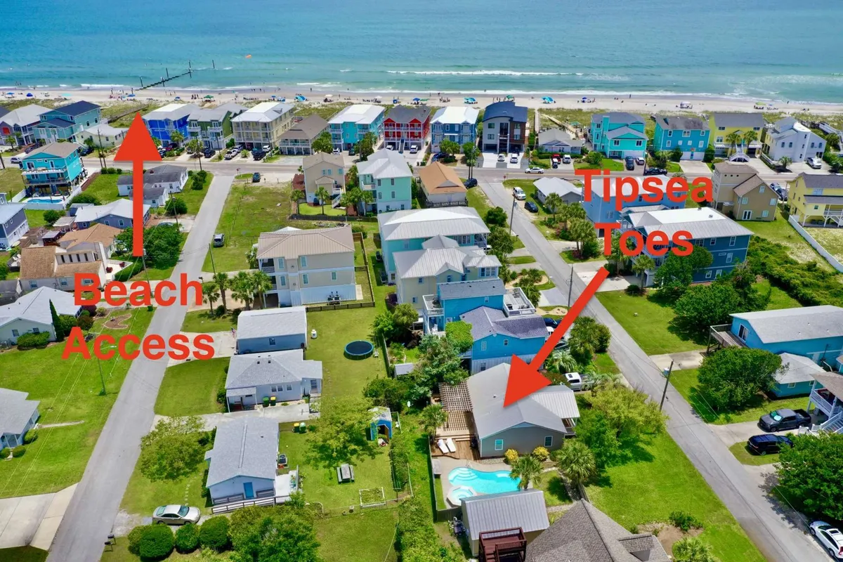 A vibrant exterior view showing direct beach access, a swimming pool area, the Tipsea Toes restaurant, and colorful beach houses. The scene captures people relaxing by the pool, walking to the beach, and enjoying the lively, inviting atmosphere.