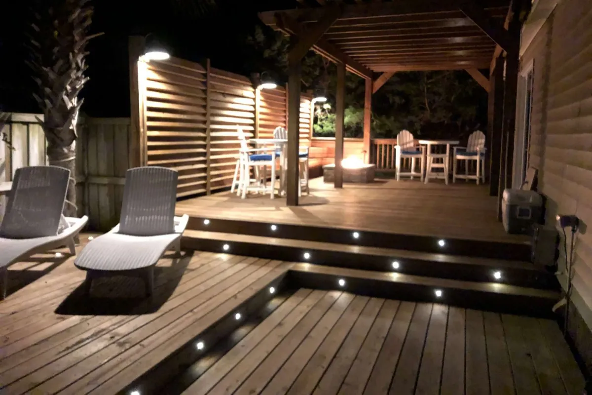 A cozy wooden deck with outdoor seating, a fire pit, decorative lighting, and palm trees—all set against the backdrop of sunset skies, inviting families to relax together after a day of adventure.