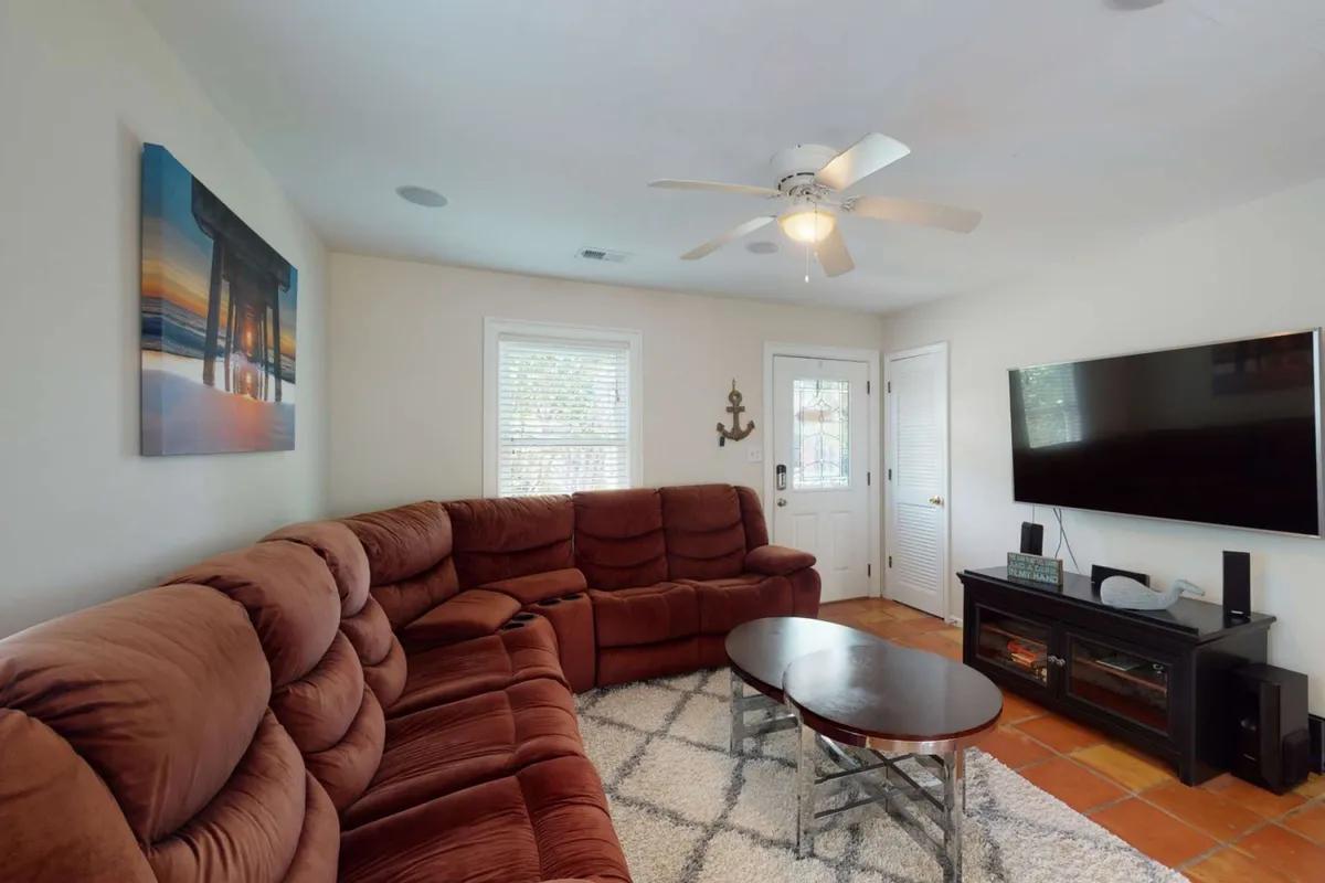 This image showcases a spacious living room area with a large sectional sofa as the centerpiece, complemented by a coffee table and a TV mounted on the wall. Artworks adorn the walls, and the overall setup is oriented for both relaxation and entertainment, providing a welcoming space for family gatherings and movie nights.