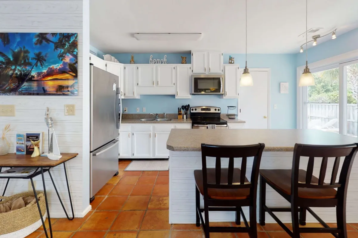 This image captures a modern kitchen with a prominent kitchen island, stainless steel appliances, and beach-themed artwork. The space is well-lit and inviting, clearly set up for both cooking and entertaining.