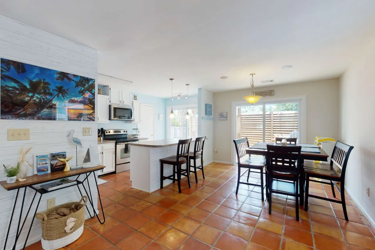 This image features a bright and cheerful dining area with a dining table, kitchen island, wall art, and an open window letting in natural light. The space is clearly meant for shared meals and social interactions, seamlessly blending dining and kitchen functions.