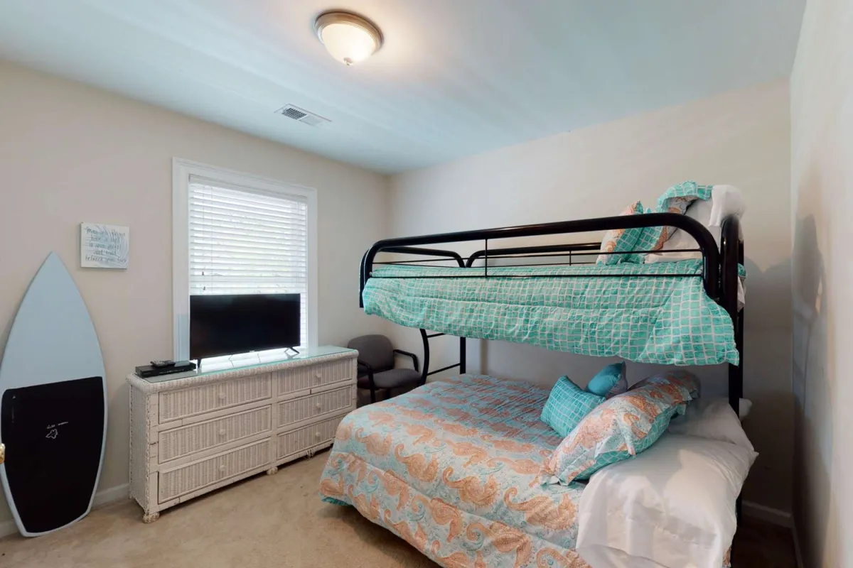 A playful bunk bedroom with a full/twin bunk bed, surfboard decor, television, and dresser. The room is inviting and kid-friendly, providing a cozy nook for children’s adventures and sleepovers.